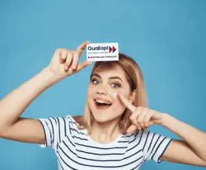 certification qualiopi décret du 31 mai 2023 capcert. Image représentant une jeune femme aux cheveux courts avec un air étonné tendant au-dessus de sa tête une petite carte sur lequel nous retrouvons le logo Qualiopi.